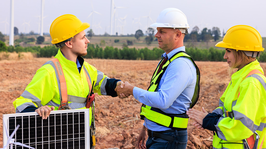 Engineer team standing shake hands in the meeting planing project install solar panel in the wind turbines farm. renewable energy installation project for the future world concept.